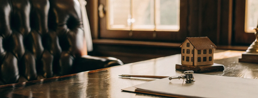 Real estate attorney's desk with a contract and house model for determining closing fees.