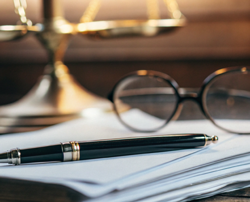 A pen on a legal contract with scales of justice, defining what makes a contract legally binding.