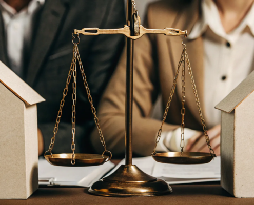Two model houses balanced on scales of justice under the Partition of Real Property Act.